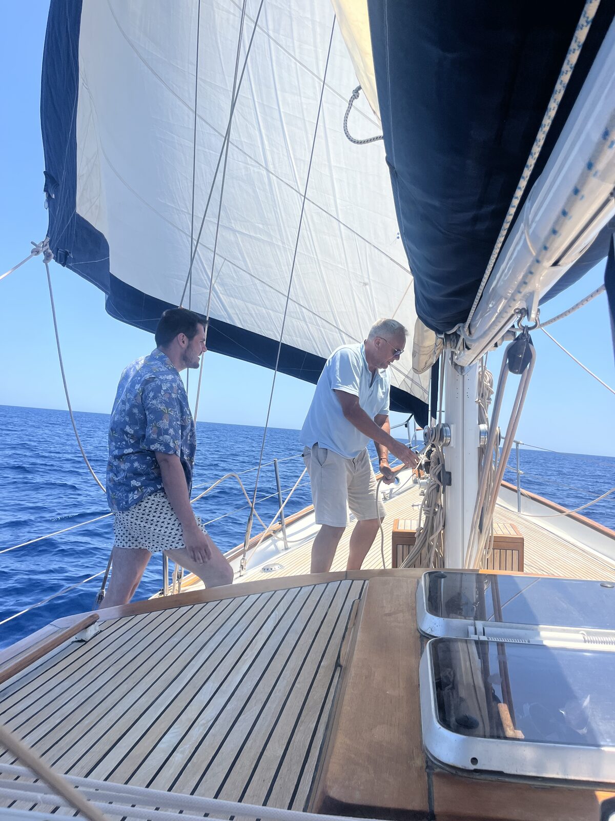 Crew working the foredeck aboard Gran Blau, rocky coastline behind